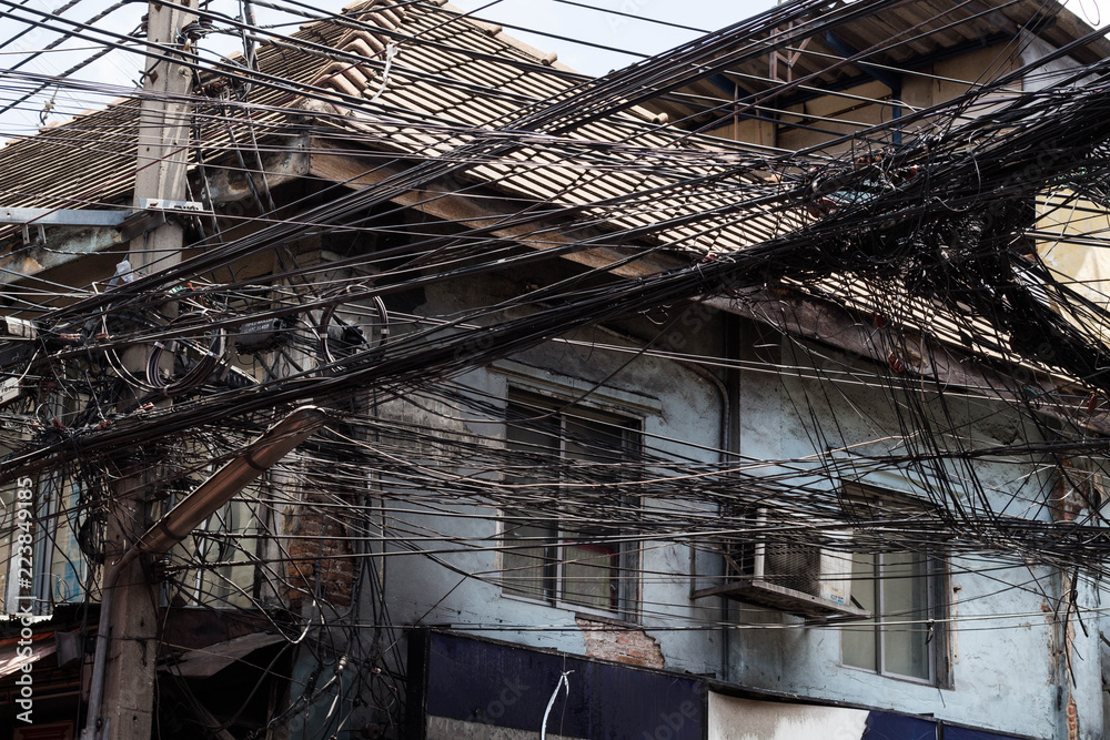 Messy electrical cables unsafe near old house. Messy electrical cables unsafe near old house.