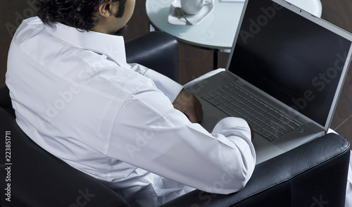 Mideastern man using laptop at office, with a cup of cofee and documents photo