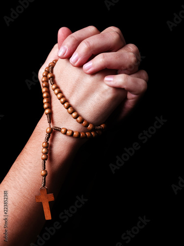 Female hands praying holding a beads rosary with a cross or Crucifix on black background. Woman with Christian Catholic religious faith. Profile or side view