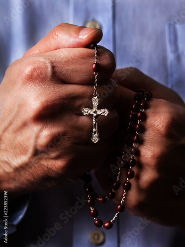 Male hands praying holding a beads rosary with Jesus Christ in the cross or Crucifix on black background. Mature man with Christian Catholic religious faith