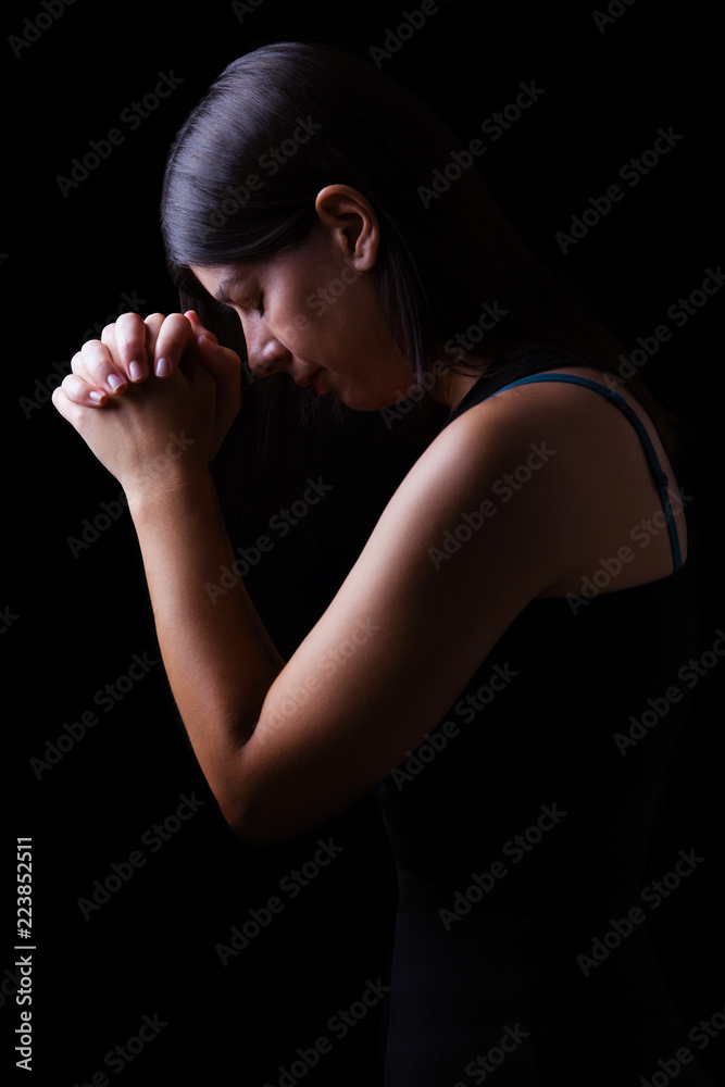 Faithful woman praying, hands folded in worship to god with head down and eyes closed in religious fervor, on a black background. Concept for religion, faith, prayer and spirituality. Faithful woman praying, hands folded in worship to god with head down and eyes closed in religious fervor, on a black background. Concept for religion, faith, prayer and spirituality.