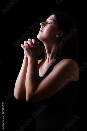 Faithful woman praying, hands folded in worship to god with head up and closed eyes in religious fervor, on a black background. Concept for religion, faith, prayer and spirituality.