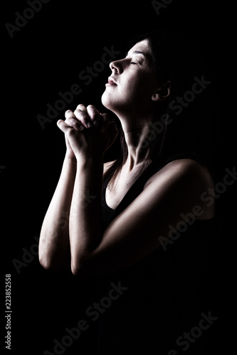 Faithful woman praying, hands folded in worship to god with head up and closed eyes in religious fervor, on a black background. Concept for religion, faith, prayer and spirituality.