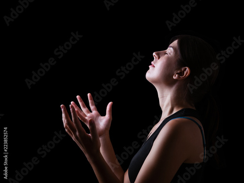 Low key of a faithful woman praying and feeling the presence or being touched by god. Arms outstretched in worship, head up and eyes closed in religious fervor. Black background.