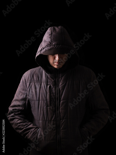 Scary and creepy caucasian or white man hiding in the shadows, with the face and identity hidden with the hood, and standing in the darkness. Low key, black background. Concept for fear, danger,