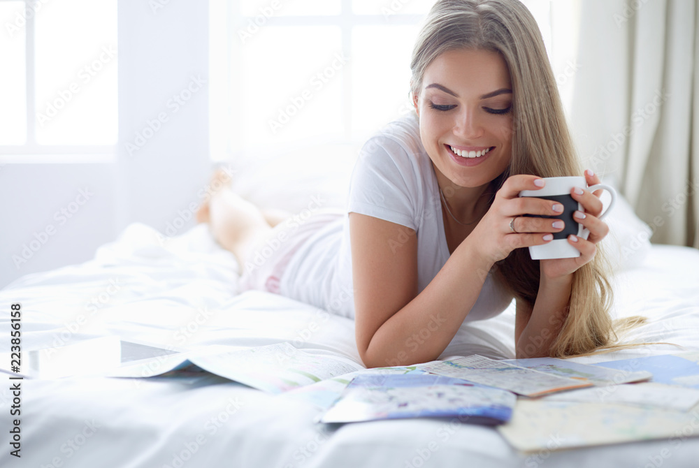 Relaxed young woman sitting on bed with a cup of coffee and digital tablet