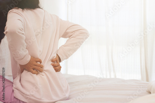 Asian woman back pain and sit on bed in bedroom in the morning.color tone