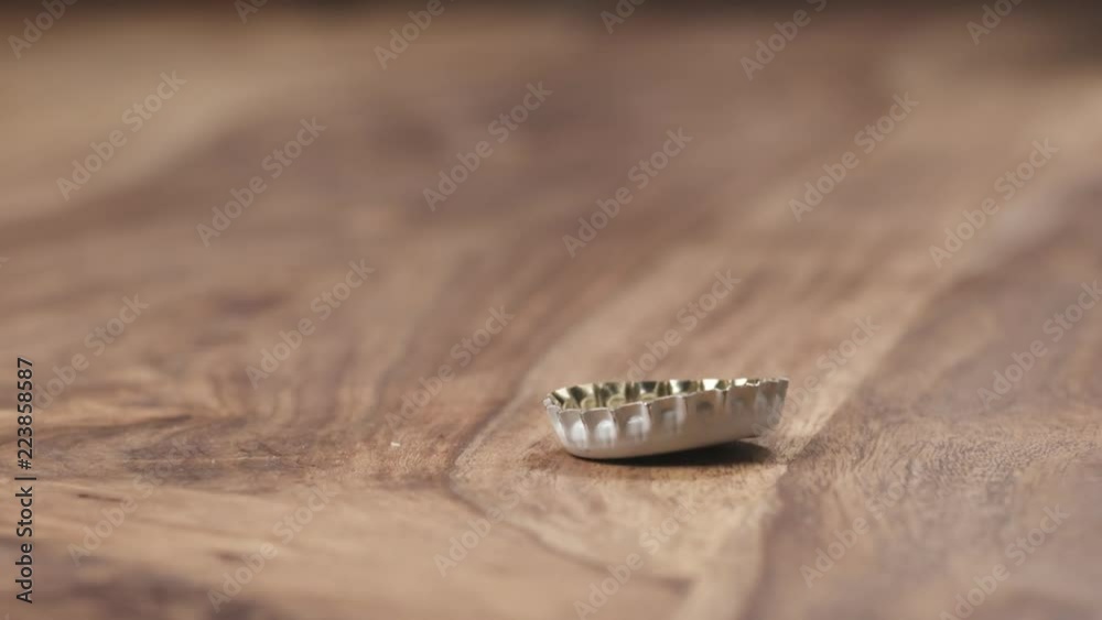 Slow motion closeup of bottle cap falling on wood table Slow motion closeup of bottle cap falling on wood table