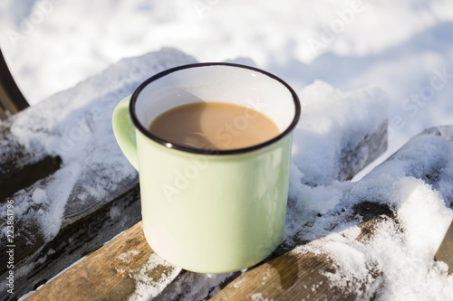 green cup of coffee on wooden rustic bench in the winter forest.