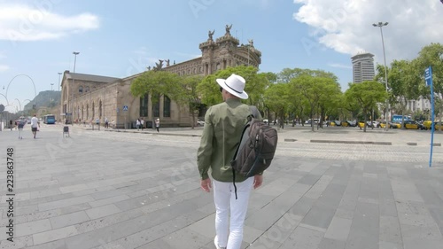 A young man, tourist walking with a backpack and in a hat near the Columbus Monument, port area on del Portal de la Pau  