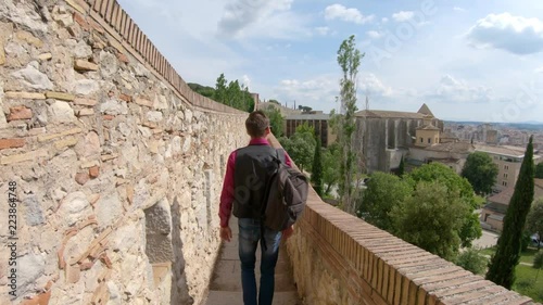A young guy with a backpack, a tourist, walks along the fortress wall in Girona, Spain. Fortress wall (Passeig de la Murala) in Girona, Spain. 