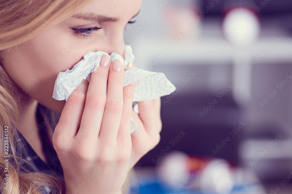 Young Caucasian woman siitng on sofa with running nose and tissues. Concept of illness and resting. Young Caucasian woman siitng on sofa with running nose and tissues. Concept of illness and resting.