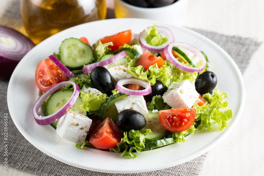 Fresh Greek salad made of cherry tomato, ruccola, arugula, feta, olives, cucumbers, onion and spices. Caesar salad in a white bowl on wooden background. Healthy organic diet food concept.