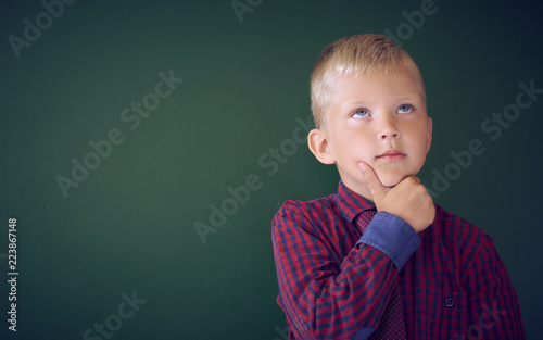 Closeup shot of schoolboy thinking with hand on chin isolated on blackboard. Portrait of pensive child thinking about his academic future.