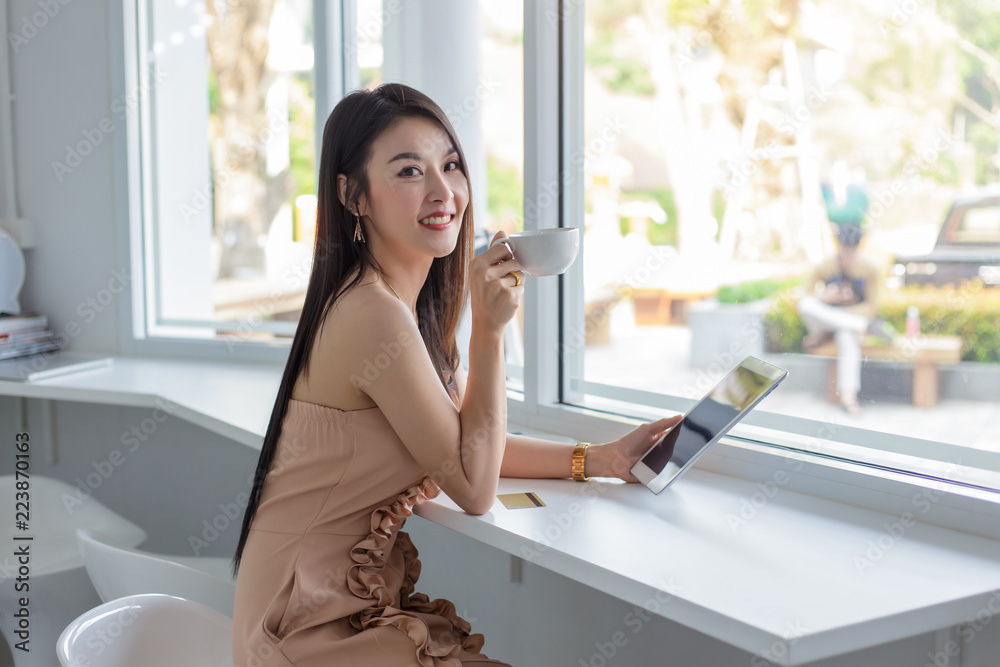 Young asian woman sitting drinking coffee and using tablet at coffee shop.