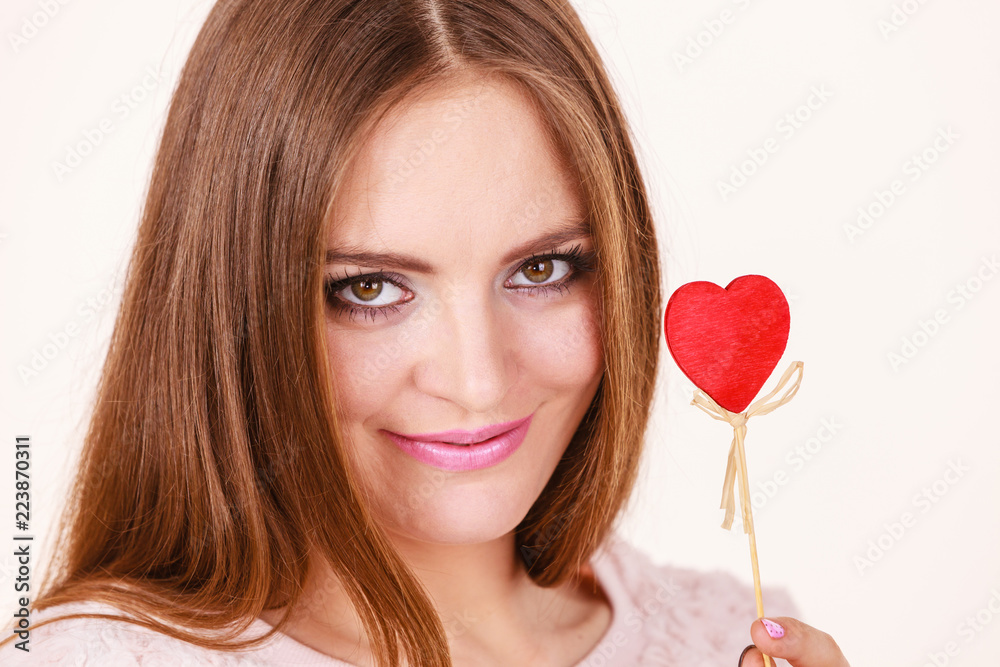 Flirty woman holding red wooden heart on stick