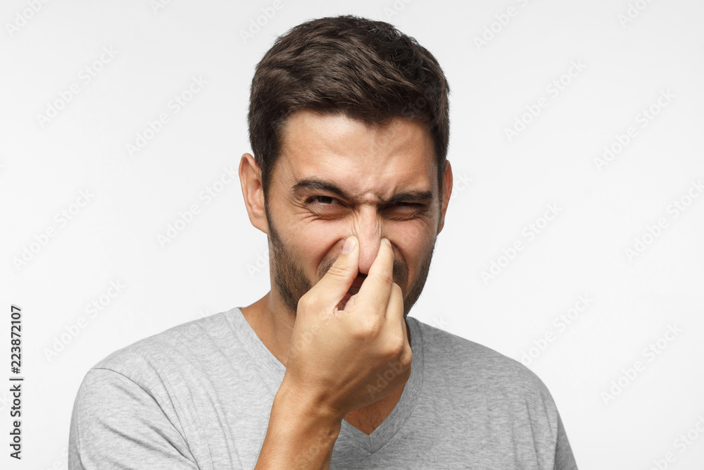 Close up portrait of young man holding his nose as if smelling something rotten and stinky, trying to find source of odor Close up portrait of young man holding his nose as if smelling something rotten and stinky, trying to find source of odor