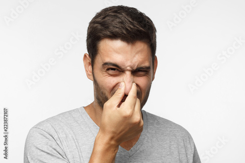 Photography Close up portrait of young man holding his nose as if smelling something rotten