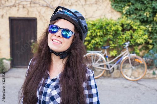 Happy woman with helmet and sunglasses posing backgound bicycle and street photo