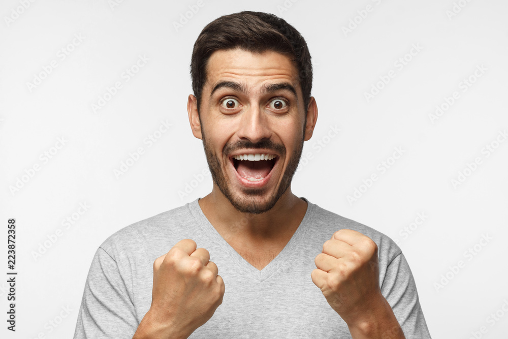 Young man shouting while his team win, raised both fist in victory gesture, isolated on gray background. Casual soccer fan concept Young man shouting while his team win, raised both fist in victory gesture, isolated on gray background. Casual soccer fan concept