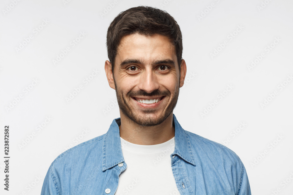 Headshot of young handsome man isolated on gray background, wearing casual blue shirt, smiling happily and friendly at camera Headshot of young handsome man isolated on gray background, wearing casual blue shirt, smiling happily and friendly at camera