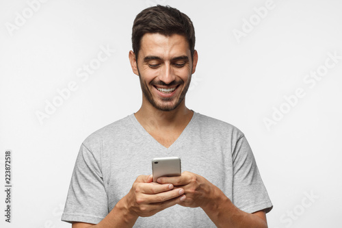 Closeup photo of young man looking at screen of smart phone, smiling nicely while chatting with friend