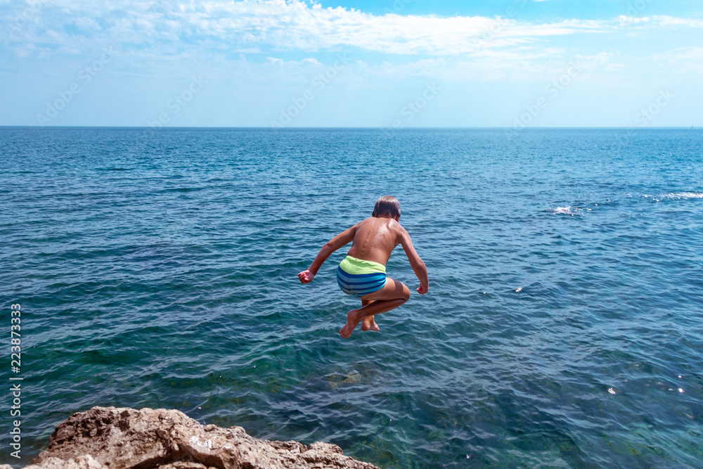 A boy is jumping from the cliff into the sea on a hot summer day. Holidays on the beach. The concept of active tourism and recreation A boy is jumping from the cliff into the sea on a hot summer day. Holidays on the beach. The concept of active tourism and recreation