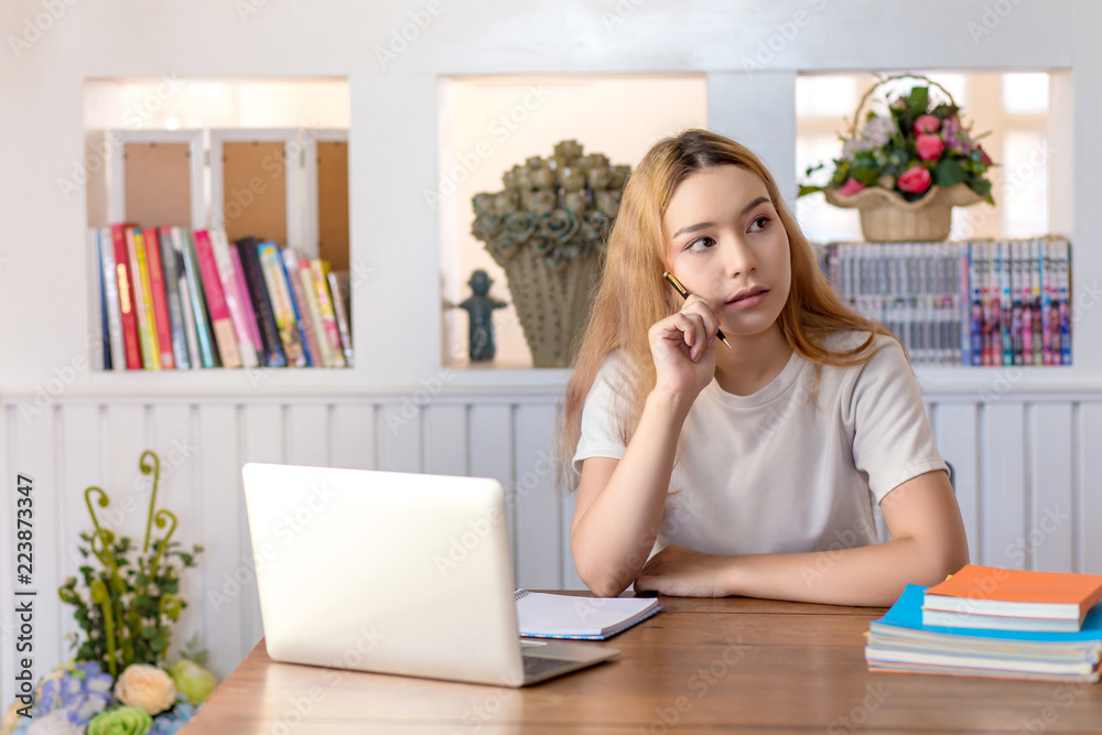 Young woman student thinking and working on laptop sitting in library at home