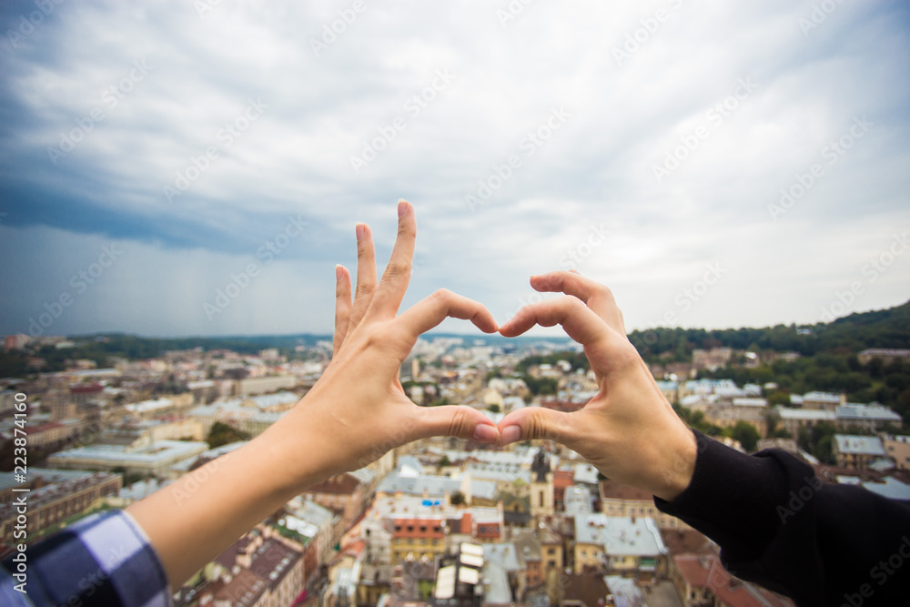 Couple hands in form of heart against old european city. Hands in shape of love heart with dramatic sky Couple hands in form of heart against old european city. Hands in shape of love heart with dramatic sky
