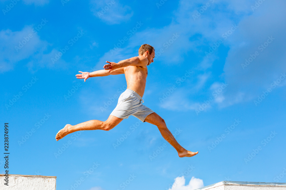 young man doing parkour jump on the blue sky background on sunny summer day young man doing parkour jump on the blue sky background on sunny summer day