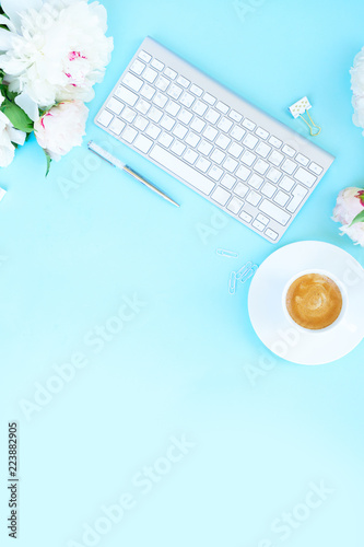 Flat lay home office workspace background with white modern keyboard and peony flowers, copy space on blue background