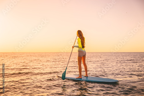 Young woman floating at stand up paddle board with warm sunset colors