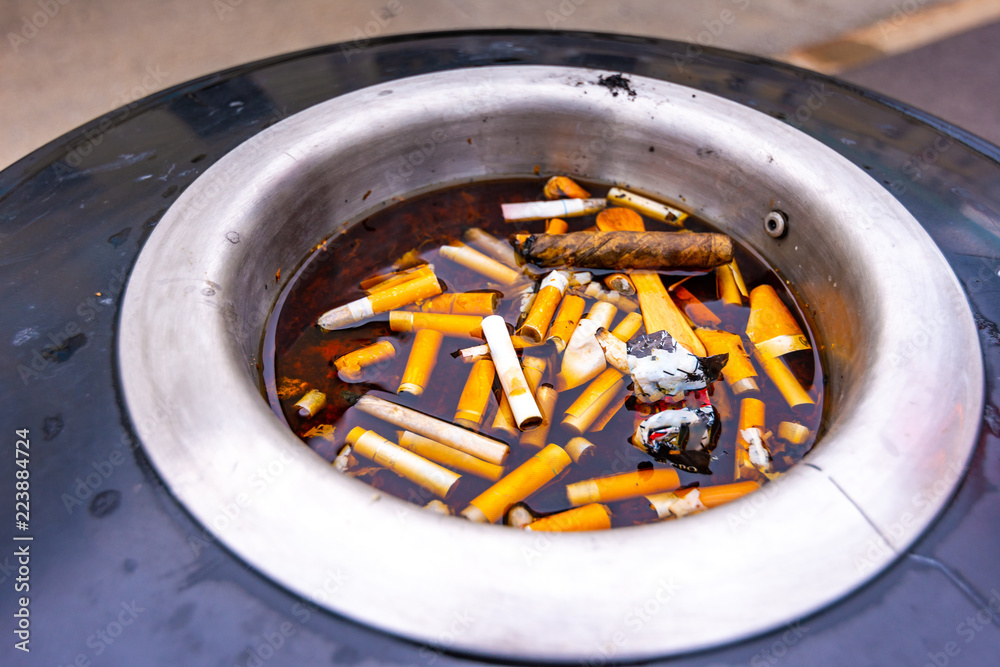 Closeup view of cigarette trash on top of recycle bin. Cigarettes are in water. Disgusting