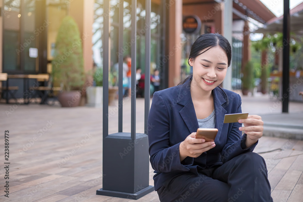 Young woman smiling. Business woman holds credit card and using smartphone. Online shopping concept Young woman smiling. Business woman holds credit card and using smartphone. Online shopping concept