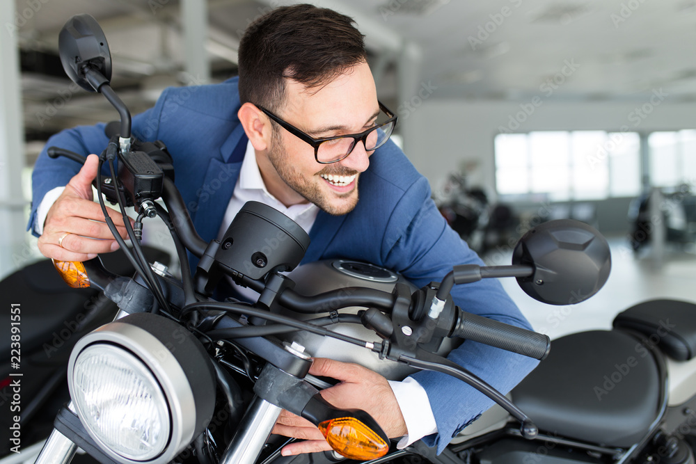 Fototapeta premium Young happy handsome man choosing a new motorcycle at motorcycle showroom.
