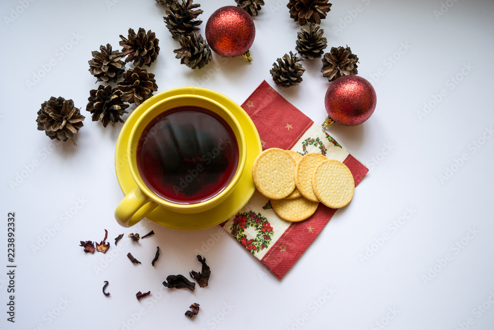 New year and christmas composition of yellow cup of hibiscus tea, Christmas tree cones, tea box and red decorations isolated on white background. New year and christmas composition of yellow cup of hibiscus tea, Christmas tree cones, tea box and red decorations isolated on white background.