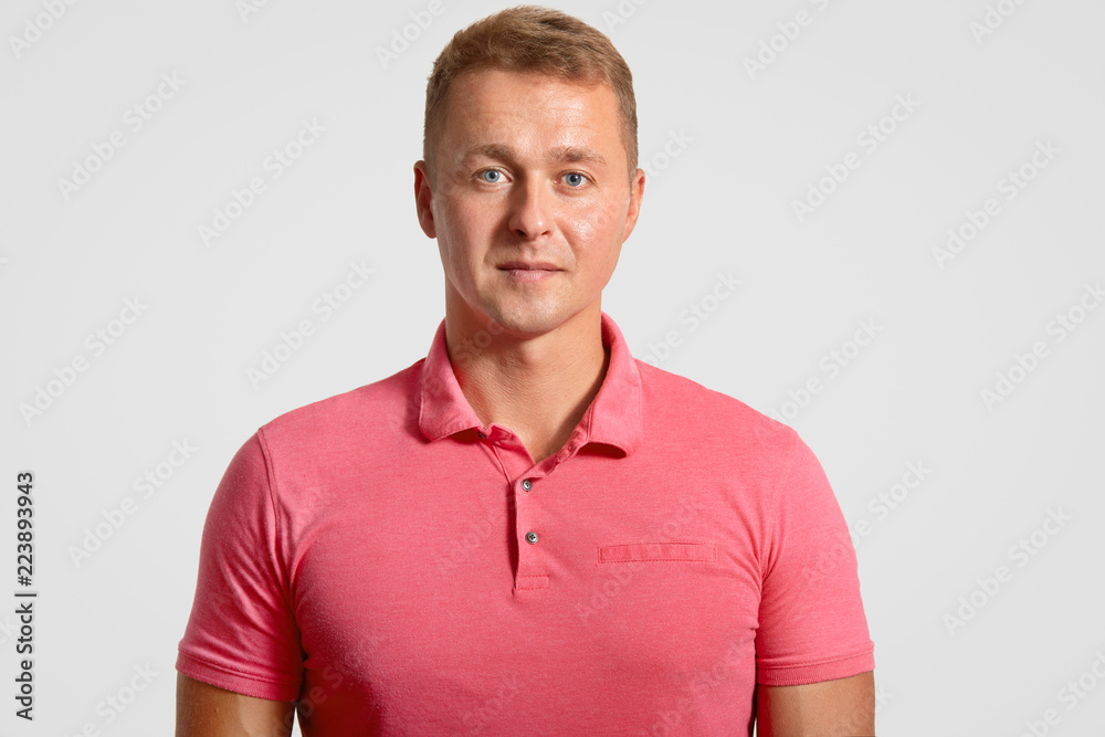 Headshot of attractive handsome man has appealing look, dressed in casual pink t shirt, ooks seriously at camera, isolated over white background. People, facial expressions and masculinity concept Headshot of attractive handsome man has appealing look, dressed in casual pink t shirt, ooks seriously at camera, isolated over white background. People, facial expressions and masculinity concept