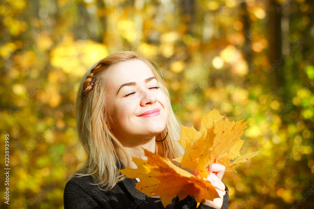 Happy young woman in park on sunny autumn day. Cheerful beautiful girl in gray sweater outdoors on beautiful fall day. Happy young woman in park on sunny autumn day. Cheerful beautiful girl in gray sweater outdoors on beautiful fall day.