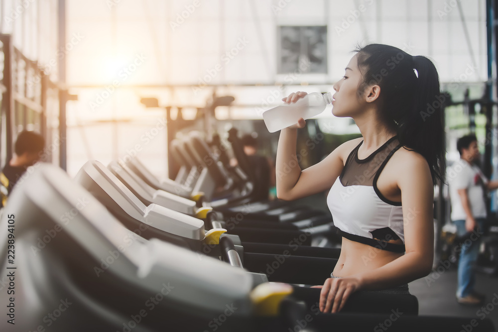 Woman drinking water after workout exercising in the gym Woman drinking water after workout exercising in the gym