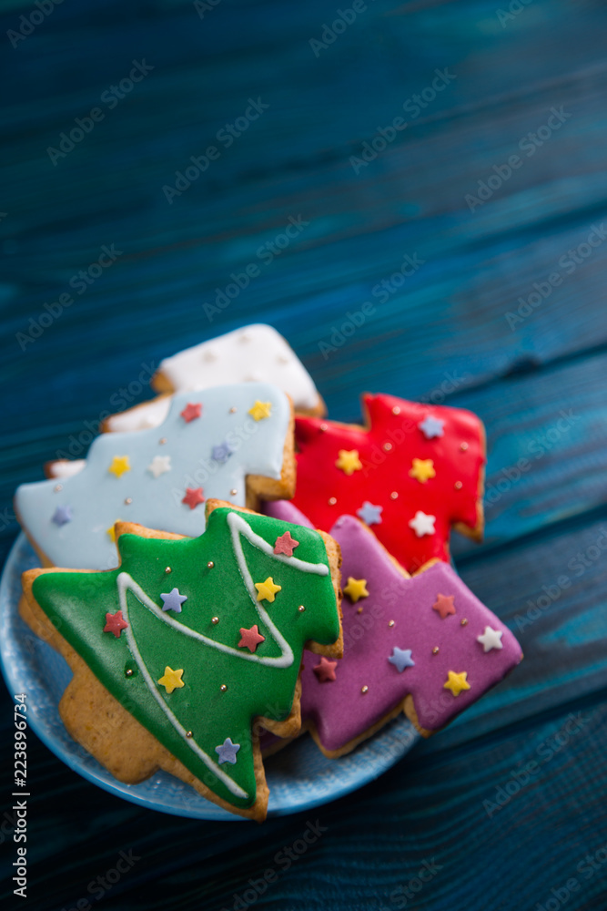 Four homemade glazed gingerbread in form of Christmas tree decorated with stars on plate on wooden table.