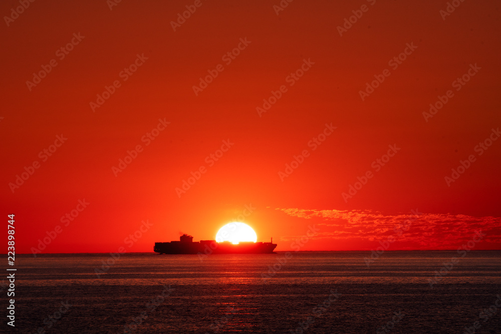 Silhouette of a container ship passing by on the horizon at sunset orange light. Skagen, Grenen in North Jutland in Denmark, Skagerrak, North Sea, Baltic Sea