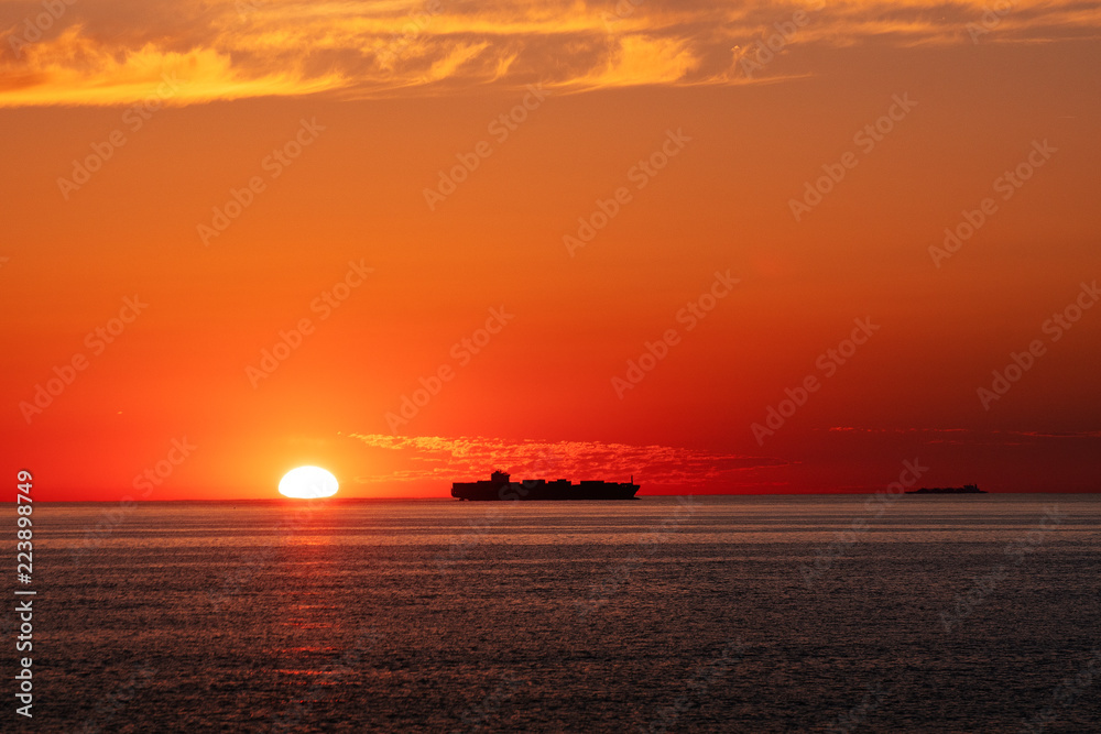 Silhouette of a container ship passing by on the horizon at sunset orange light. Skagen, Grenen in North Jutland in Denmark, Skagerrak, North Sea, Baltic Sea