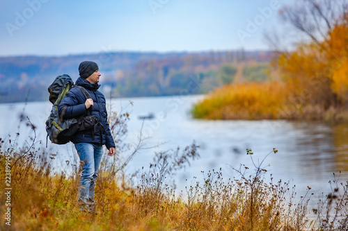a tourist with a backpack looks at the other bank of the river in the autumn. A traveler walks in cold weather