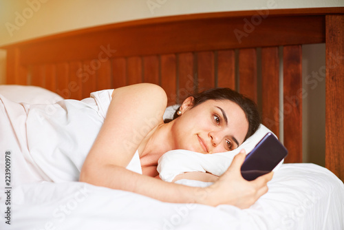 Woman laying in bed with smrtphone photo