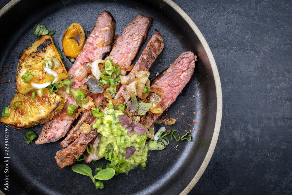Modern style barbecue dry aged wagyu flank steak with pineapples and chimichurri sauce as top view on a plate with copy space right