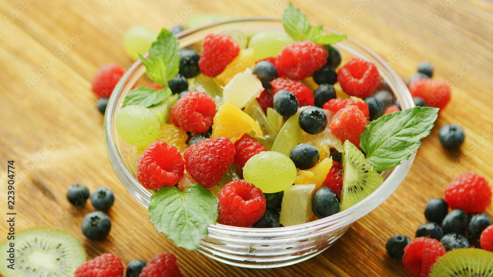 From above glass bowl full of mixed fruit salad on wooden table From above glass bowl full of mixed fruit salad on wooden table