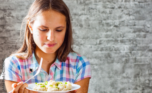 portrait of young teenager brunette girl with long hair eating Meat dumplings on gray wall background
