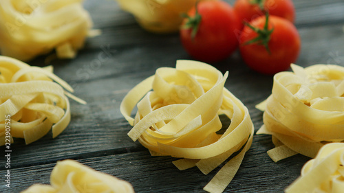Tagliatelle rolled in balls with ripe red tomatoes placed near on wooden background