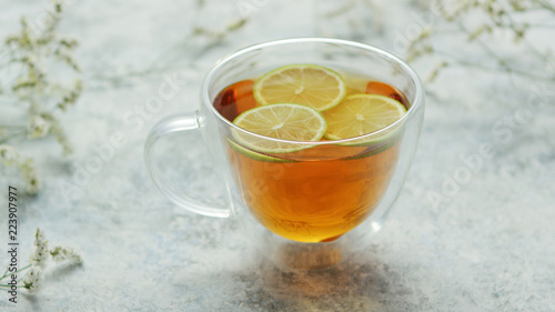 From above view of glass mug with brown tea and lemon on white background of tablecloth