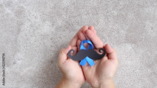 Mustache pattern with blue ribbon symbol in child's hands. Movember concept. Prostate Cancer and men's health awareness.